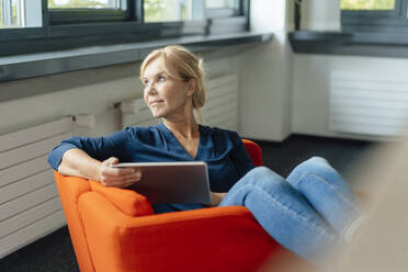 Thoughtful businesswoman holding tablet PC on armchair in office - JOSEF15271