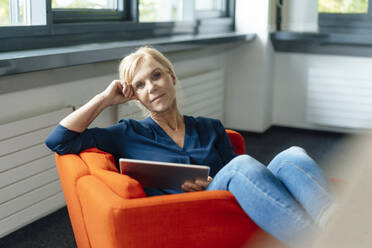 Mature businesswoman holding tablet computer on armchair in office - JOSEF15273