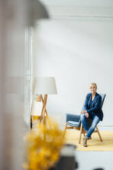 Businesswoman sitting on armchair in front of white wall - JOSEF15283