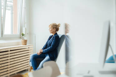 Thoughtful businesswoman looking through window at workplace - JOSEF15284