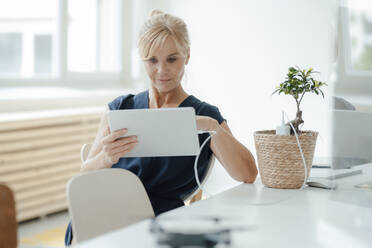 Geschäftsfrau mit Tablet-PC, der durch eine Topfpflanze im Büro aufgeladen wird - JOSEF15294