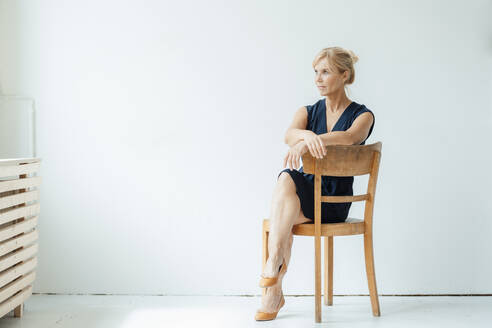 Ältere Geschäftsfrau sitzt auf einem Stuhl vor einer weißen Wand - JOSEF15296