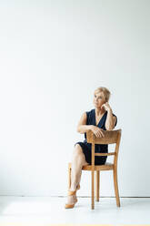 Geschäftsfrau sitzt auf einem Stuhl vor einer weißen Wand - JOSEF15297