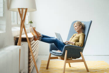 Mature businesswoman using laptop on armchair in office - JOSEF15311