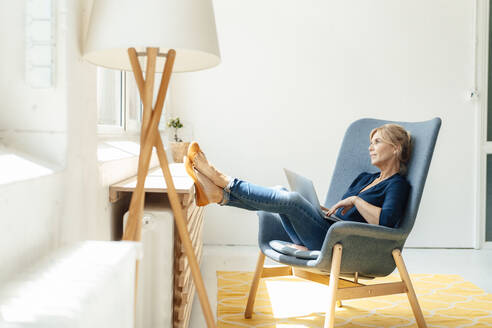 Nachdenkliche reife Geschäftsfrau mit Laptop auf einem Sessel - JOSEF15326