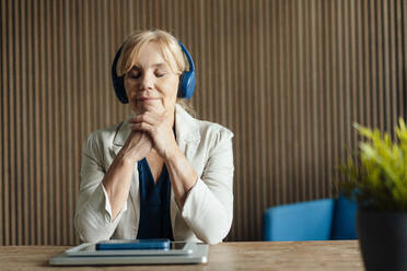 Reife Geschäftsfrau, die mit drahtlosen Technologien auf dem Schreibtisch Musik hört - JOSEF15358