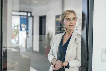 Thoughtful businesswoman in office seen through glass door - JOSEF15369