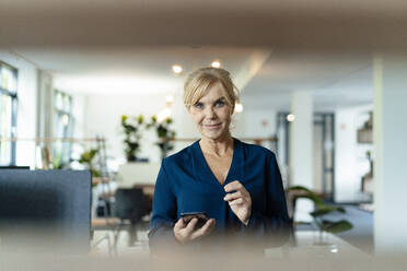 Lächelnde Geschäftsfrau mit Mobiltelefon am Arbeitsplatz - JOSEF15380