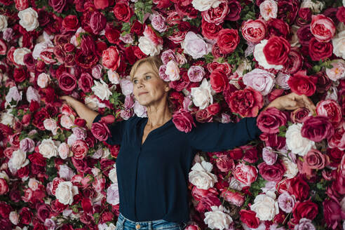 Businesswoman leaning with arms outstretched on flower wall - JOSEF15383