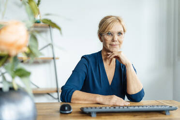 Contemplative businesswoman wearing eyeglasses at desk in office - JOSEF15388