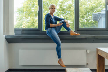 Geschäftsfrau mit Mobiltelefon auf der Fensterbank im Büro sitzend - JOSEF15396