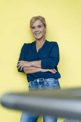 Lächelnde Geschäftsfrau mit verschränkten Armen vor einer gelben Wand lehnend - JOSEF15407