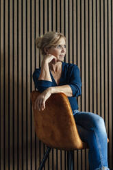 Nachdenkliche Geschäftsfrau sitzt auf einem Sessel vor einer gestreiften Wand - JOSEF15418