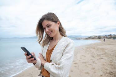 Lächelnde schöne junge Frau mit Smartphone am Strand - JOSEF15441