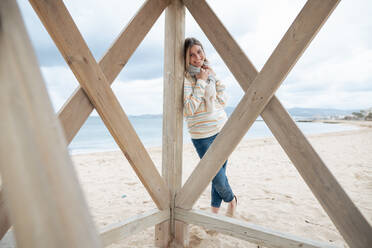 Smiling woman leaning on wooden lifeguard hut at beach - JOSEF15442