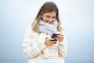 Smiling blond young woman using smart phone at beach - JOSEF15473