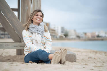Lächelnde junge Frau, die sich an eine hölzerne Rettungsschwimmerhütte lehnt, um am Strand zu träumen - JOSEF15474