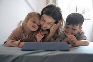 Lächelnde junge Frau mit Kindern, die im Schlafzimmer zu Hause einen Tablet-PC benutzen - JOSEF15519