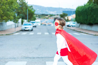 Seitenansicht eines kleinen Mädchens in Superheldenkostüm und Maske auf einem Zebrastreifen in der Stadt - ADSF41961