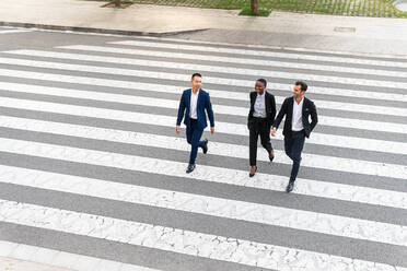 From above full body of cheerful diverse coworkers in formal clothes walking along pedestrian crossing and chatting on street - ADSF41999