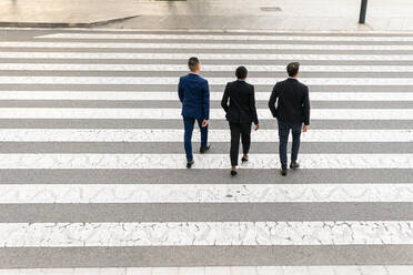 From above full body back view of diverse coworkers in formal clothes walking along pedestrian crossing and chatting on street - ADSF42001