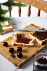 Hoher Winkel von appetitlichen knusprigen Toasts mit Kirschmarmelade auf hölzernen Schneidebrett in der Nähe von frischen reifen Kirschen auf dem Tisch serviert - ADSF42028