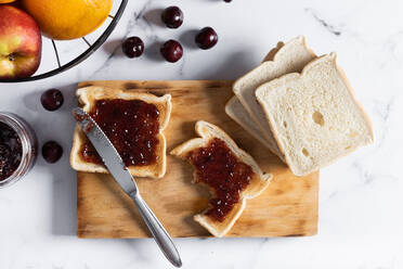 Hoher Winkel von appetitlichen knusprigen Toasts mit Kirschmarmelade auf hölzernen Schneidebrett in der Nähe von frischen reifen Kirschen auf dem Tisch serviert - ADSF42029