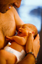 Side view of smiling bearded father standing in room and gently holding infant baby in diaper - ADSF42031