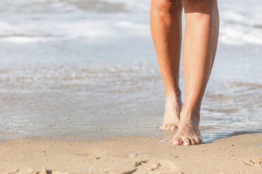 Crop anonyme barfuß Frau zu Fuß auf Sandstrand entlang winken Meerwasser - ADSF42048