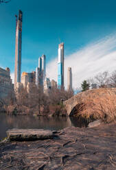 Gapstow Bridge überquert ruhigen Teich gegen Wolkenkratzer und bewölkten blauen Himmel im Central Park von New York, USA - ADSF42064