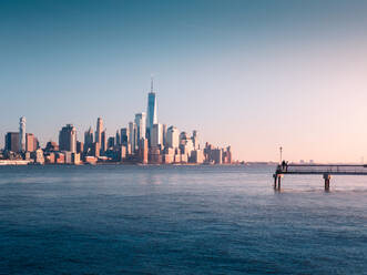 High rise building of Manhattan located on shore of New York Bay with pier against cloudless sunset sky - ADSF42066