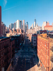 Drone Blick auf leere Asphaltstraße geht in der Nähe von Wohnhäusern gegen Wolkenkratzer und wolkenlosen blauen Himmel in Manhattan, New York, USA - ADSF42068