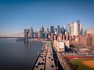 Drohnenansicht von Autos auf dem FDR Drive am Ufer des East River in der Nähe der Brooklyn Bridge und von Wolkenkratzern gegen einen wolkenlosen blauen Himmel am Abend in Manhattan, New York, USA - ADSF42069