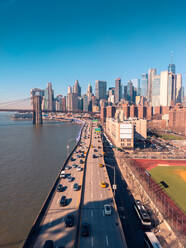 Drone view of cars driving on FDR Drive on shore of East River near Brooklyn Bridge and skyscrapers against cloudless blue sky in evening in Manhattan, New York, USA - ADSF42071