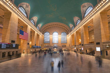 Menschen gehen in der Halle des Grand Central Terminal mit USA-Flagge hängen zwischen Säulen in New York - ADSF42076