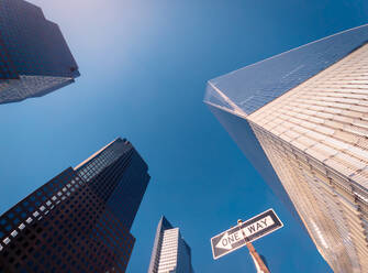 Von unten Wolkenkratzer in der Nähe von One Way Zeichen gegen wolkenlosen blauen Himmel auf sonnigen Tag auf der Straße von New York, USA - ADSF42082
