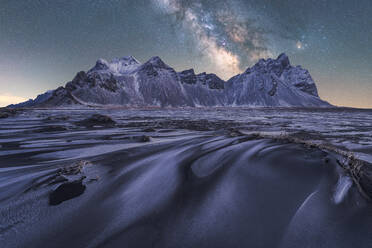 Landschaftlicher Blick auf gefrorenen Strand gegen verschneite Berge im Winter Abend in Island mit sternenreichen Milchstraße Himmel - ADSF42099