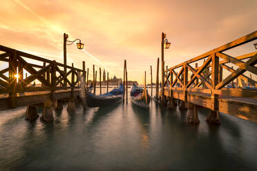Traditionelle Gondeln, die in der Nähe der hölzernen Kais im Becken von San Marco vor dem bewölkten Himmel bei Sonnenuntergang in Venedig, Italien, festgemacht sind - ADSF42150