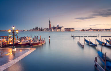 Eine Reihe traditioneller Gondeln, die in der Nähe des Piers im Becken von San Marco vor San Giorgio Maggiore auf einer Insel an einem bewölkten Abend in Venedig, Italien, festgemacht sind - ADSF42152