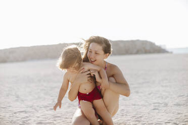 Glückliche Mutter mit hemdsärmeligem Jungen, der sich am Strand vergnügt - MDOF00369