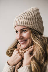 Happy blond woman wearing knit hat against white background - JOSEF15526