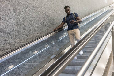Mann, der ein Mobiltelefon benutzt, fährt auf einer Rolltreppe nach unten - TAMF03798
