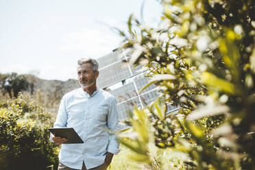 Mature man standing with tablet PC in front of solar panels - JOSEF15547