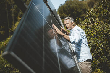 Mature man examining solar panels on sunny day - JOSEF15548