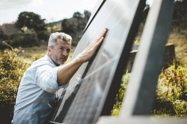 Älterer Mann berührt Sonnenkollektoren im Garten - JOSEF15549