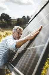Älterer Mann berührt Sonnenkollektoren im Garten an einem sonnigen Tag - JOSEF15552