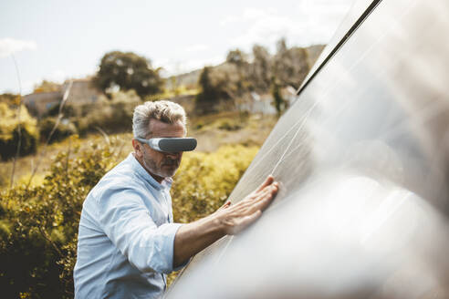 Älterer Mann mit VR-Brille berührt Solarpanel im Garten - JOSEF15562