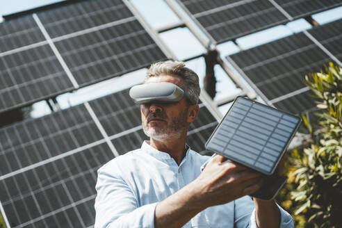 Älterer Mann mit VR-Brille hält Solarpanel im Garten - JOSEF15569