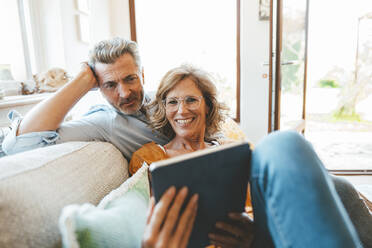 Mature couple using tablet PC sitting on sofa in living room - JOSEF15609