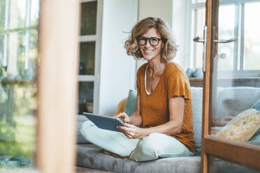 Lächelnde reife Frau sitzt mit Tablet-PC zu Hause - JOSEF15617